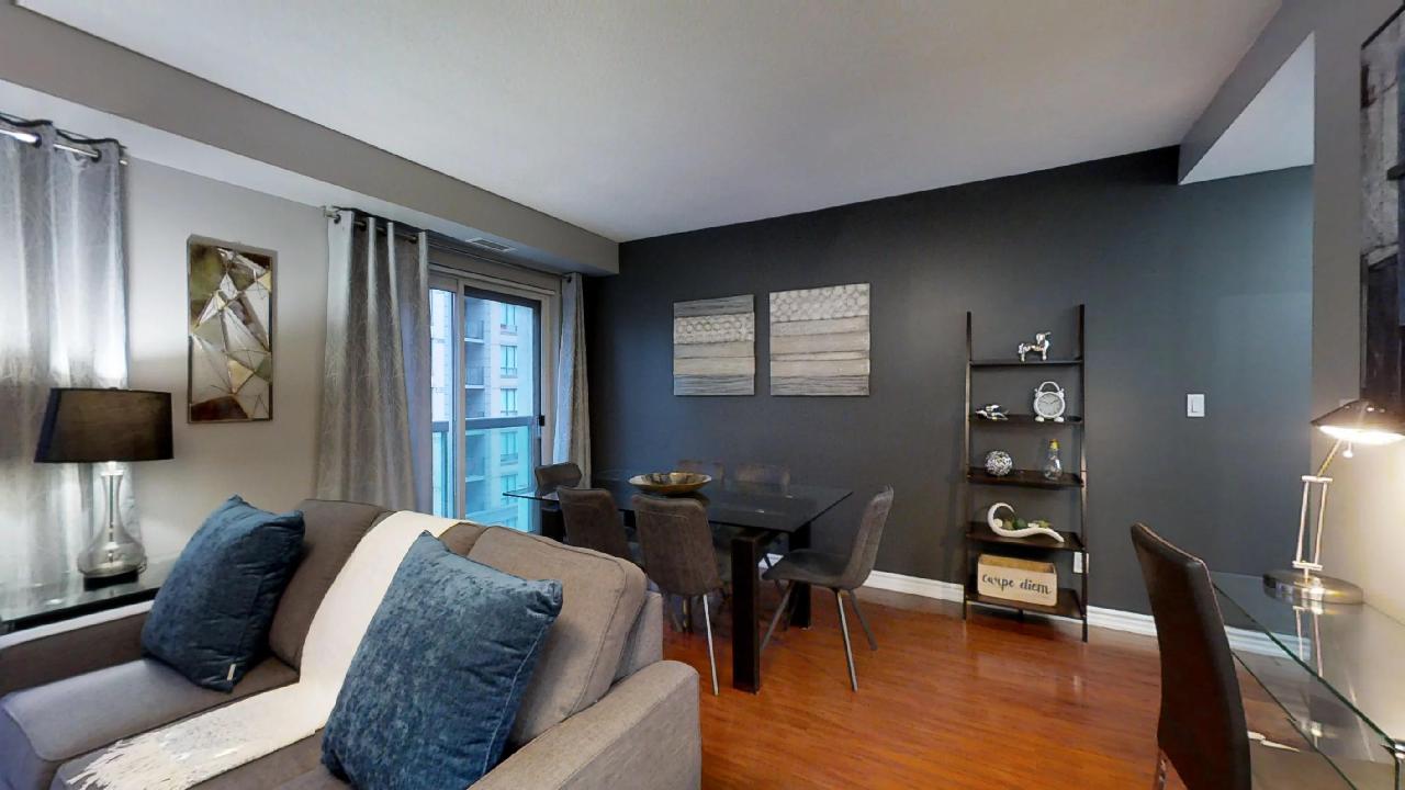 the living room and dining area in a toronto furnished apartment, featuring gray walls and a blue pillow