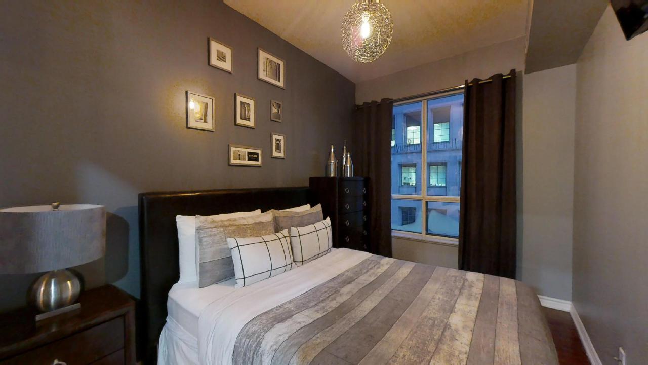 A bed featuring grey sheets in a furnished unit in Toronto, near the Entertainment district
